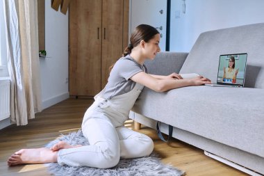 Evdeki kanepede yatan psikologla çevrimiçi terapi seansında genç bir bayan. Terapist danışmanıyla sanal görüşmede dizüstü bilgisayar kullanan genç bir kız. Psikoloji, akıl sağlığı, ergenlik kavramı.