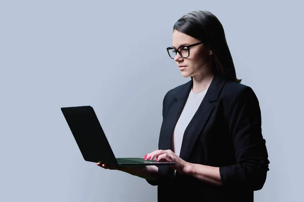 Młoda Bizneswoman Używająca Laptopa Szarym Tle Studia Poważna Pewna Siebie — Zdjęcie stockowe
