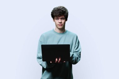 Laptop kullanan genç bir üniversite öğrencisi, beyaz stüdyo geçmişi var. Kameraya bakan gülümseyen yakışıklı adam. İnternet teknolojileri, çevrimiçi öğrenim istirahatı, sanal uzaktan eğitim eğlence iletişimi