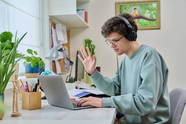 十几岁的男大学生坐在耳机里 举行视频电话会议 坐在家里的桌子旁看着笔记本电脑上的摄像头 在线培训 远程虚拟课程 — 图库照片