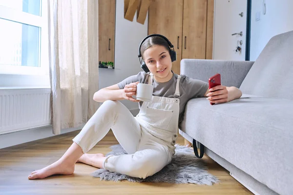Mladá Puberťačka Sluchátkách Sedí Doma Podlaze Pohovky Chytrým Telefonem Dívá — Stock fotografie