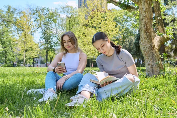Δύο Έφηβες Φίλες Χαλαρώνουν Στο Γρασίδι Χρησιμοποιώντας Βιβλίο Ανάγνωσης Smartphone — Φωτογραφία Αρχείου