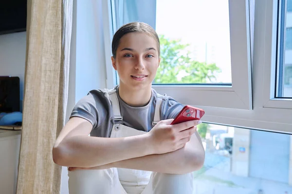Teenage Girl Sitting Home Window Smartphone Hands Looking Camera Young — Stock Photo, Image