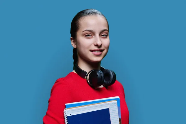 带着课本笔记本 手握蓝色工作室背景的高中女生的画像 穿着红色衣服的少女看着相机 青春期 学习概念 — 图库照片