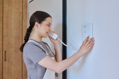 İçeride misafirlerle konuşurken dahili telefonu tutan genç bir kız.