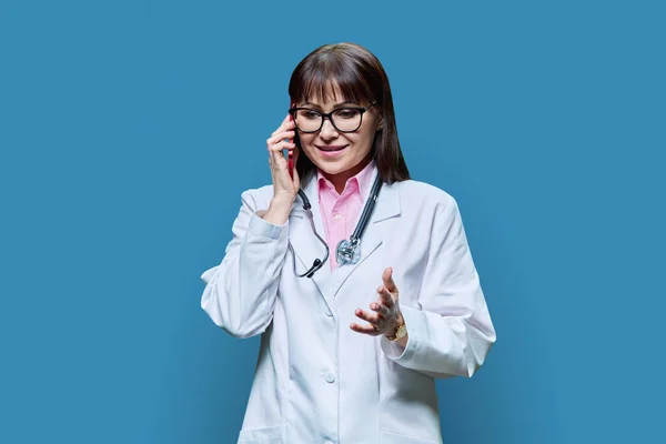 Starší Doktorka Bílém Plášti Mluví Telefonu Pozadí Modrého Studia Medicína — Stock fotografie