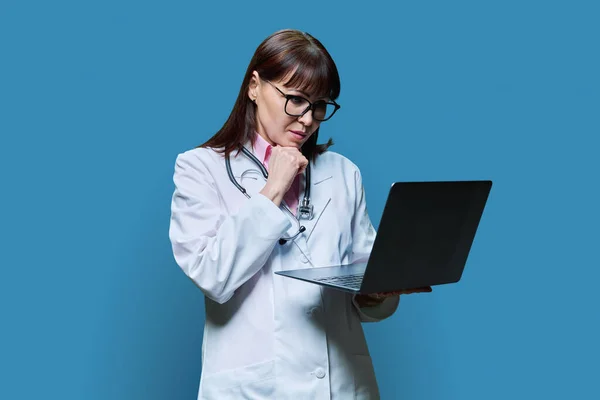 Médica Madura Usando Computador Portátil Fundo Estúdio Azul Mulher Confiante — Fotografia de Stock