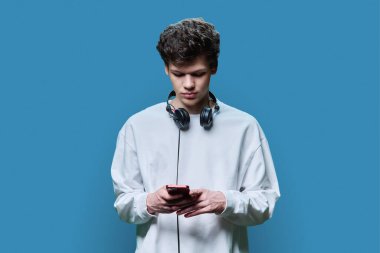 Kulaklıklı, mavi arka planda akıllı telefon kullanan genç, ciddi bir erkek. 18 yaşında, 19 yaşında bir üniversite öğrencisi. Mektup yazan bir alet arıyor. İnternet teknolojisi, mobil uygulamalar