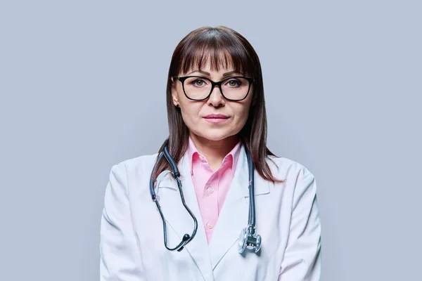 白色实验服手套听诊器中严肃中年女医生的画像 在灰色工作室背景下看着相机 医药健康保护 专业医务工作者 服务概念 — 图库照片
