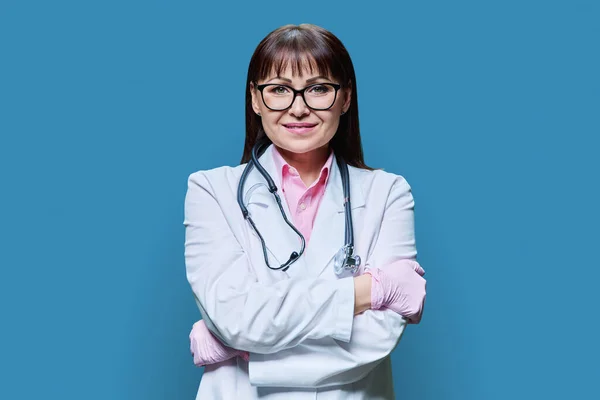 中年妇女医生的画像 身穿白色实验室外套 双臂交叉 在蓝色工作室背景下看着相机 医药健康保护 专业医务工作者 医疗服务概念 — 图库照片