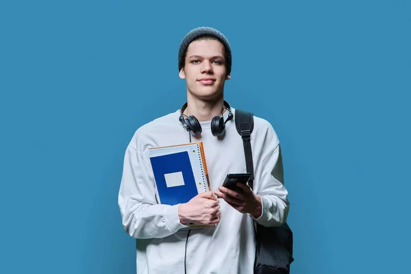 Junger Ernsthafter Mann Mit Rucksackbüchern Mit Smartphone Auf Blauem Hintergrund — Stockfoto