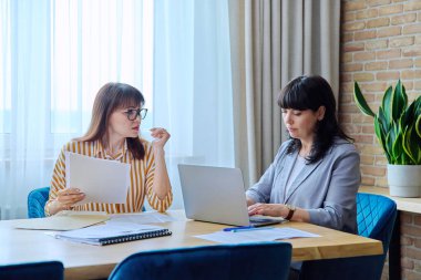 Ofisteki büyük masada oturan iki olgun iş kadını iş evrakları dizüstü bilgisayarla sözleşme imzaladı. İşletme CEO 'su hukuk finans danışmanlık danışmanlık takım çalışması, 40' lı 50 'li yılların çalışanı