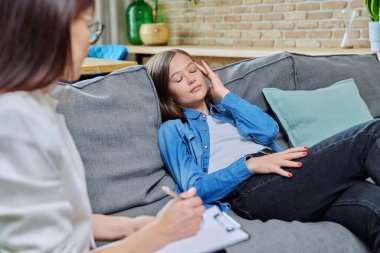 20 'li yaşlarda üzgün bir kadın koltukta oturan psikolog bir kadınla görüşüyor. Psikoloji, terapi, psikoterapi, tedavi, akıl sağlığı konsepti