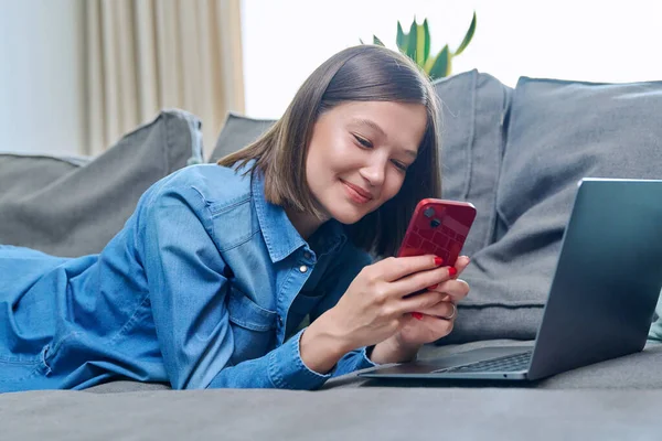 スマートフォンのラップトップを使用して若い笑顔幸せな女性は リビングルームで自宅のソファに横たわっていた インターネットオンラインサービス モバイルアプリケーション レジャー研究の仕事のライフスタイルのための技術 — ストック写真