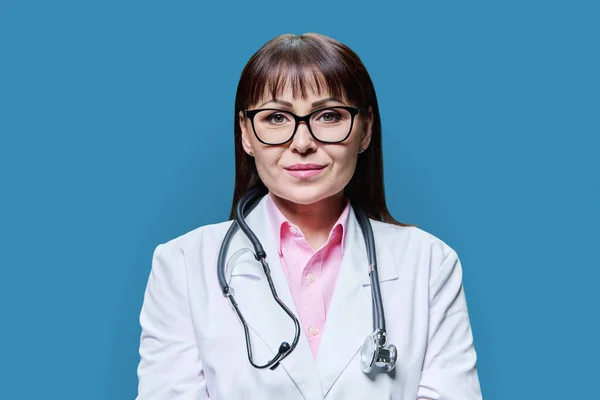 严肃的中年女医生在白色实验室外套听诊器中的画像 在蓝色工作室背景下看着相机 医药健康保护 专业医务工作者 服务概念 — 图库照片