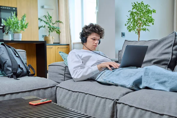 20岁的年轻人在家里休息 躺在客厅的沙发上 用耳机看笔记本电脑屏幕 互联网在线技术 研究休闲交流的概念 — 图库照片