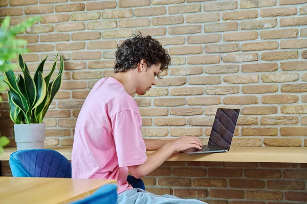 一个英俊的19 20岁的学生在笔记本电脑上打字 坐在家里的办公桌前 利用互联网在线技术进行学习 — 图库照片