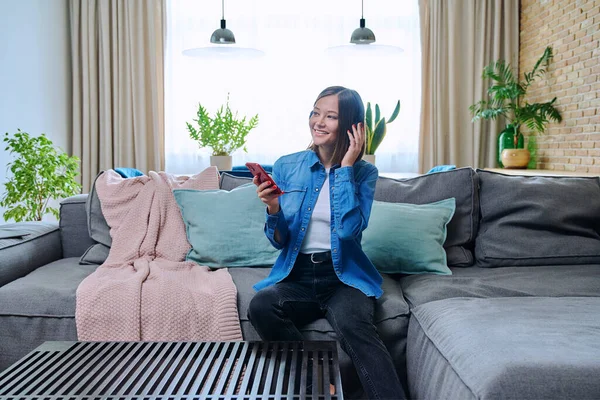 Mujer Joven Sentada Sofá Sala Estar Con Auriculares Usando Teléfono —  Fotos de Stock