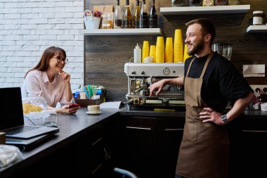 Genç erkek barista kahve dükkanında kadın müşteriyle konuşuyor, tezgahın yanında taze hazırlanmış cappuccino kahvesiyle. Küçük işletme, hizmet, kahve dükkanı, personel, iş kavramı