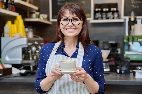 コーヒーの新鮮なカップを保持成功した女性の中小企業の所有者の肖像画 コーヒーショップカウンターの近く エプロンで中年の女性ウェイターの労働者笑顔 フードサービスの職業 スタッフ — ストック写真