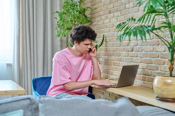 一个英俊的19 20岁的学生在笔记本电脑上打字 坐在家里的办公桌前 利用互联网在线技术进行学习 — 图库照片