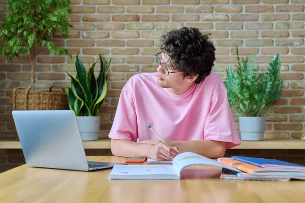 年轻的男大学生在家学习 使用笔记本电脑 一个19岁的帅哥带着眼镜在笔记本上写字 利用互联网在线技术进行学习 — 图库照片