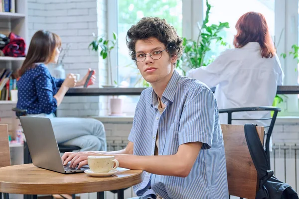 英俊的卷曲小伙子 大学生 拿着笔记本电脑杯咖啡 坐在咖啡店的桌子旁 看着相机 用于休闲 青年生活方式的互联网在线技术 — 图库照片