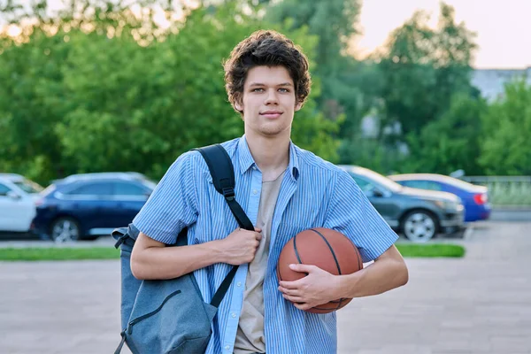 リュック付きの若い男性大学生の屋外肖像画 手にバスケットボールボール カメラを見ている中髪のハンサムな男 20歳の学生 ライフスタイルの概念 — ストック写真