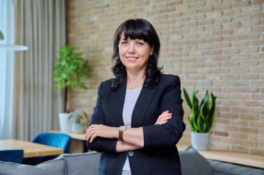 Ofiste kendine güvenen olgun bir kadının portresi. Arkadaş canlısı, başarılı, 50 'li yaşların kadın lideri, yönetici, yönetici, kollarını kavuşturup kameraya bakan yönetici. İş, kariyer, iş