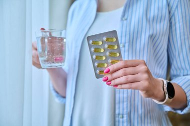 Omega 3 balık yağı kapsüllerine yaklaşırken kadınların elinde bir bardak su vardı. Besin takviyeleri diyeti, güzellik sağlığı cilt kılları, günlük yaşam tarzı, sağlık hizmetleri, vitamin d, e, a,