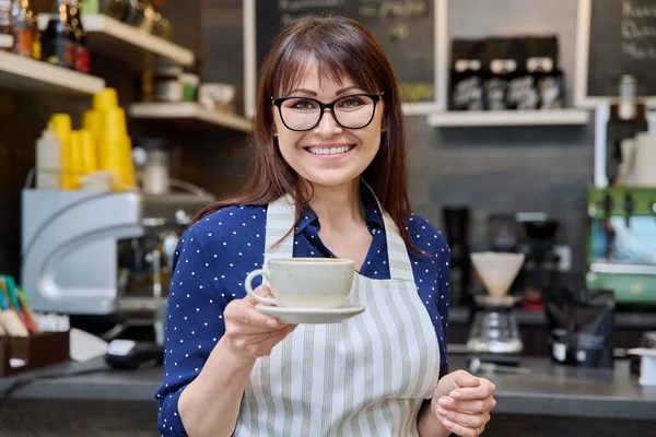 コーヒーの新鮮なカップを保持成功した女性の中小企業の所有者の肖像画 コーヒーショップカウンターの近く 中年の女性のウェイター エプロンの労働者笑顔 フードサービスの職業 スタッフ — ストック写真