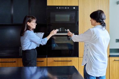 Kendine güvenen kadın emlakçı, apartman dairesini kiracıya olgun bir kadın olarak gösteriyor. Mobilyalı modern mutfağı gösteren panosu olan kadın emlakçı. Emlak satışı, kira, iş, insanlar