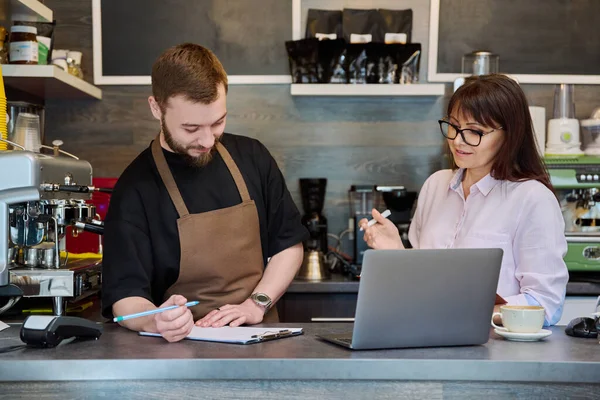 同事们 年轻的男性和成熟的女性都站在咖啡店的柜台后面用笔记本电脑聊天 小企业 团队合作 伙伴关系概念 — 图库照片
