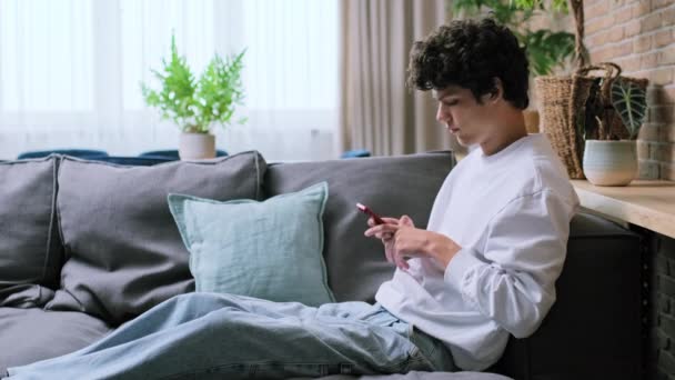 Jeune Beau Mec Utilisant Smartphone Assis Sur Canapé Dans Salon — Video