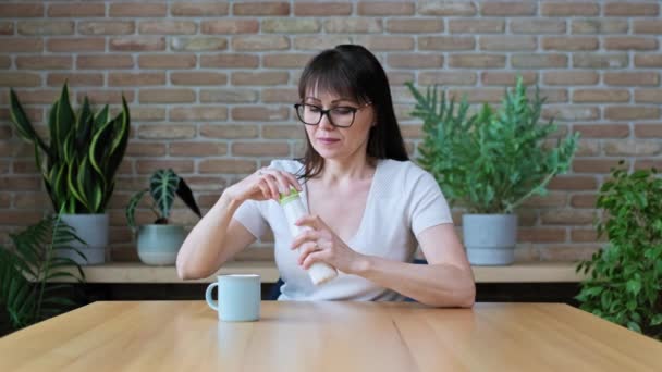 中年の女性のボトルから発酵乳製品を飲んで 自宅のテーブルのカップ 健康的な朝食にヨーグルトを注ぐに座っている 乳製品 ヨーグルト ケフィア 健康的な食事の概念 — ストック動画