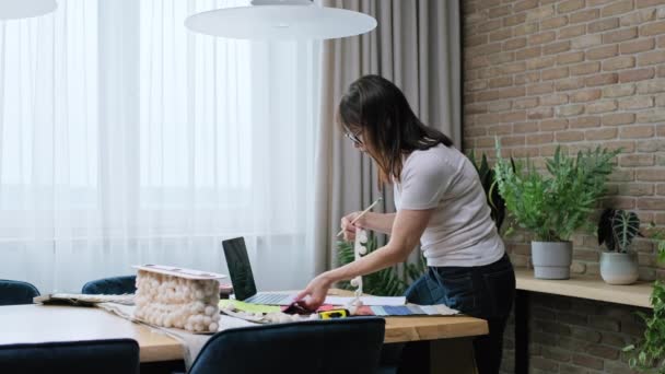 ファブリックサンプル ラップトップコンピュータで彼女の机で働いている成熟した女性のインテリアデザイナー 装飾家 繊維インテリアデザイン デザイン選択 コスト計算 — ストック動画