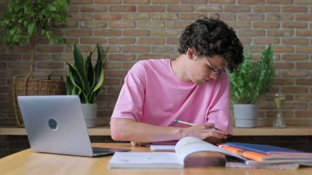 家庭でノートパソコンを使って勉強している若い男性大学生 ノートに眼鏡をかけて19歳のハンサムな男 レジャー 通信のためのインターネットオンライン技術を使用してください — ストック動画