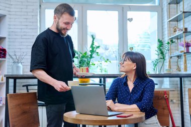 Genç bir erkek garson, kadın müşteriye kek ve kahve servisi yapan bir kafenin sahibi. Gıda hizmeti mesleği, küçük işletme, personel, iş, iş, insan kavramı