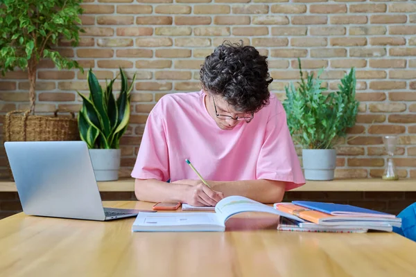 年轻的男大学生在家学习 使用笔记本电脑 一个19岁的帅哥带着眼镜在笔记本上写字 利用互联网在线技术进行学习 — 图库照片