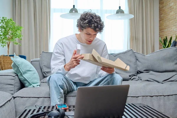 年轻的男性打开网上购物的包装 坐在沙发上 带着新智能手机的盒子 网上购物 青年概念 — 图库照片