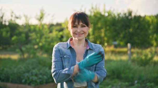 笑容满面的农妇形象 双臂交叉 种菜背景的自然田园 中年妇女戴着手套看着摄像机 小企业概念 — 图库视频影像