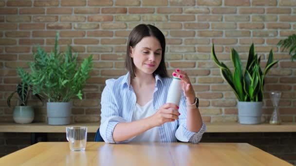 年轻女子喝着瓶装发酵乳制品 坐在桌旁 吃着健康的早餐 采购产品奶制品维生素产品 健康饮食的概念 — 图库视频影像