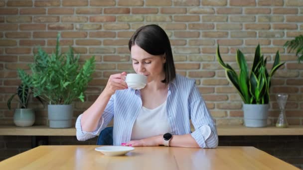 コーヒーを飲みながらリビングルームのテーブルに座っている若い女性 — ストック動画