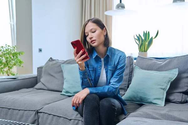 Young fashionable beautiful woman at home on couch in living room using smartphone. Internet online service, technology, mobile applications for study leisure life work shopping