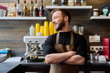 Önlüklü genç, kendine güvenen erkek kahve dükkanı sahibinin portresi. Kamera ve kahve makinesi arkaplanına bakıyor. Küçük işletme girişimcisi yemek servisi işgali personeli