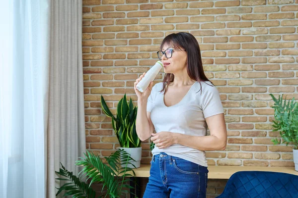 中年の女性のボトルから発酵乳製品を飲んで 窓の近くの自宅で 健康的な朝食 乳製品 ヨーグルト ケフィア 健康的な食事の概念 — ストック写真