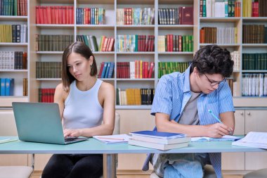Genç erkek ve bayan öğrenciler üniversite kütüphanesinde masalarında oturuyorlar, ellerinde kitaplar, defterler, çalışmalar, sınavlara hazırlanmalar. Bilgi, eğitim, gençlik, üniversite konsepti