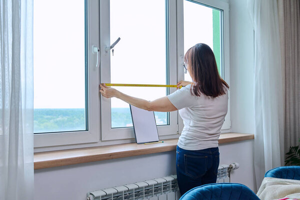Woman measuring window with tape measure, tailoring service. Tailoring service, hanging curtains, roller blinds