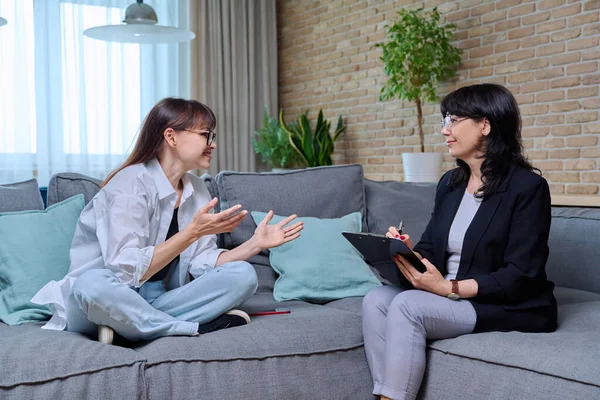 Orta yaşlı bir kadın psikolog danışmanıyla görüşüyor, koltukta oturuyor. Ruhsal sorunları olan bir kadın, psikolojik destek. Psikoloji psikoterapi tedavisi, sağlık hizmetleri.