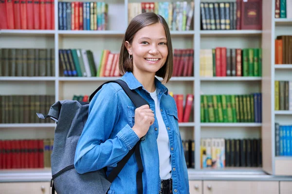 年轻微笑的女大学生背着背包看着相机 在教学楼的图书馆里 大学概念 — 图库照片